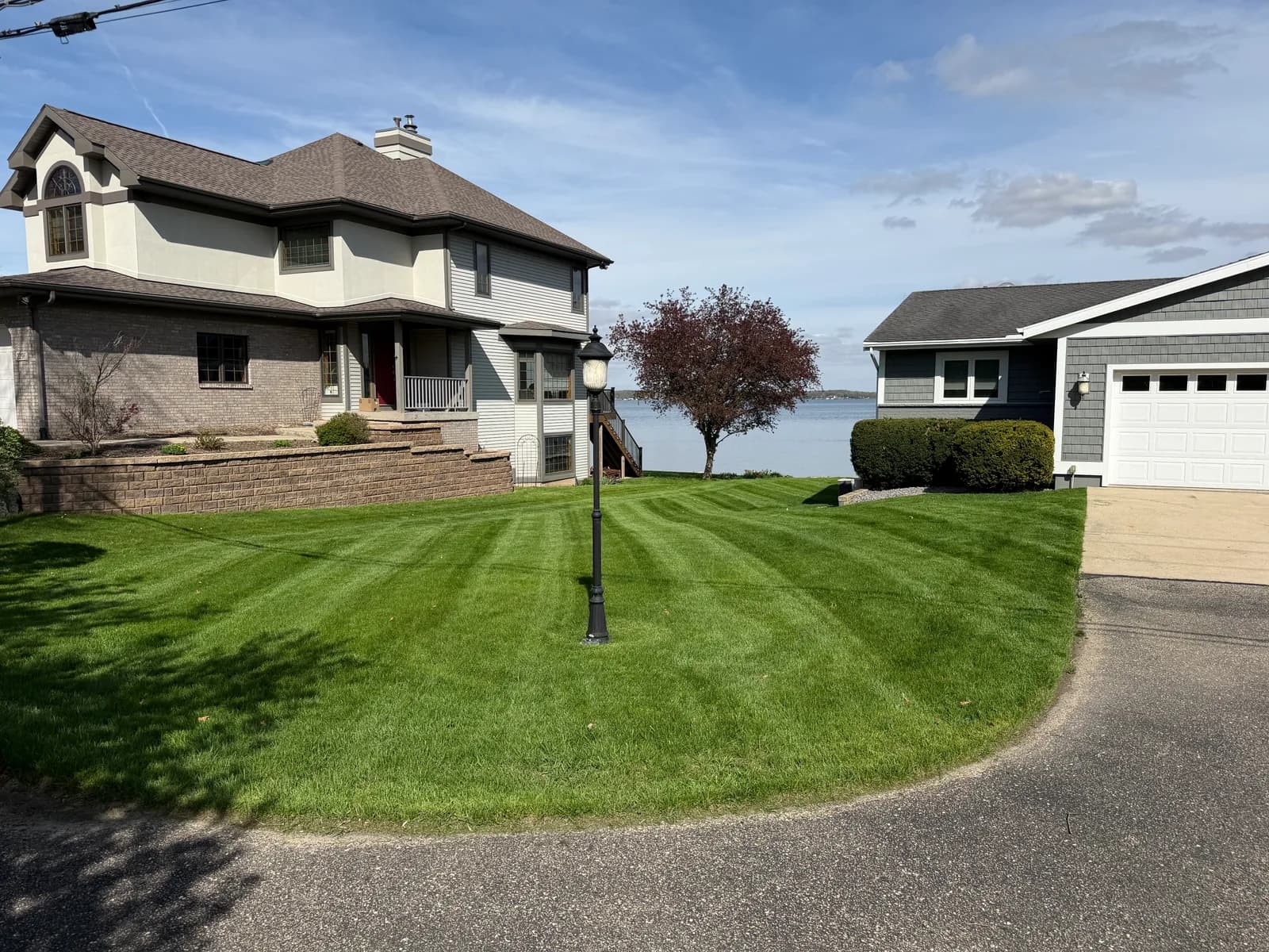 The same lakefront lawn after mowing, cut in straight stripes with a clean edge along the driveway